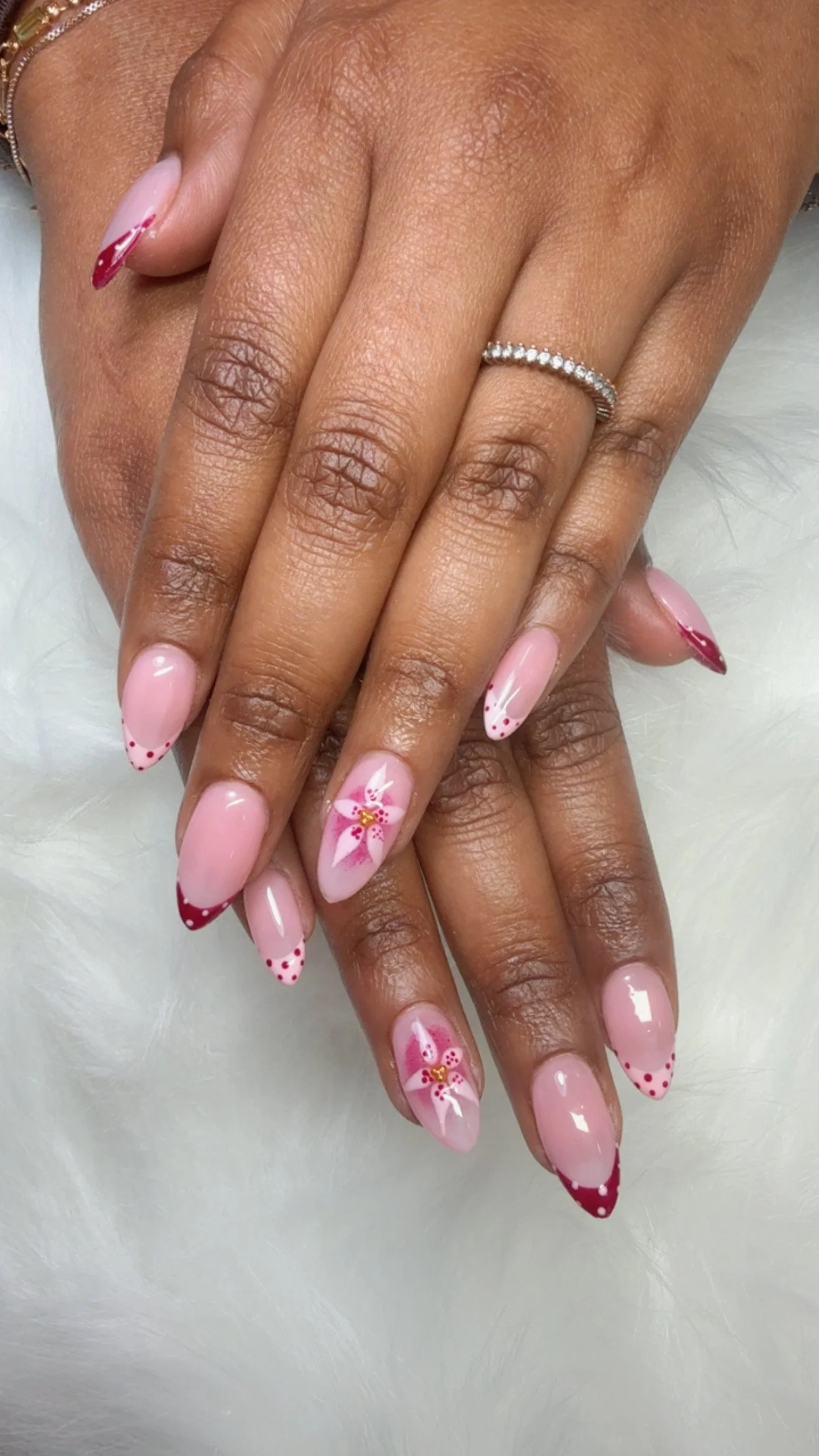 Close-up of hands with manicured nails featuring pink and red French tips and floral designs, with a ring on one finger.