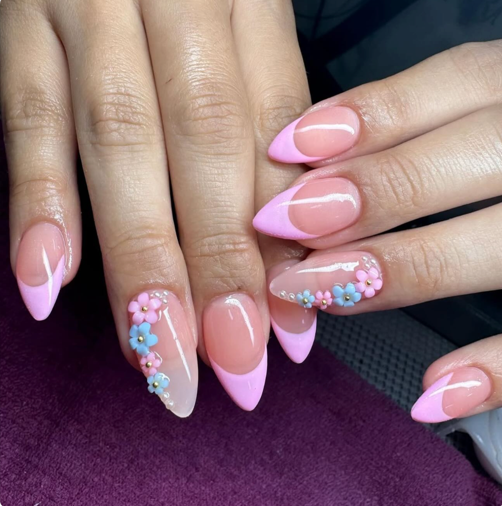 Close-up of a hand with manicured nails featuring pink and white French tips and floral 3D nail art with pink and blue flowers.