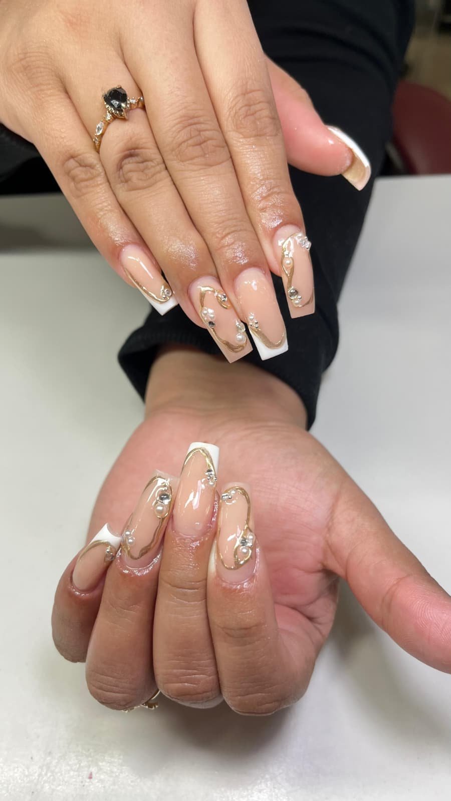 Close-up of two hands with elaborate manicured nails and jewelry, resting on a light-colored surface.