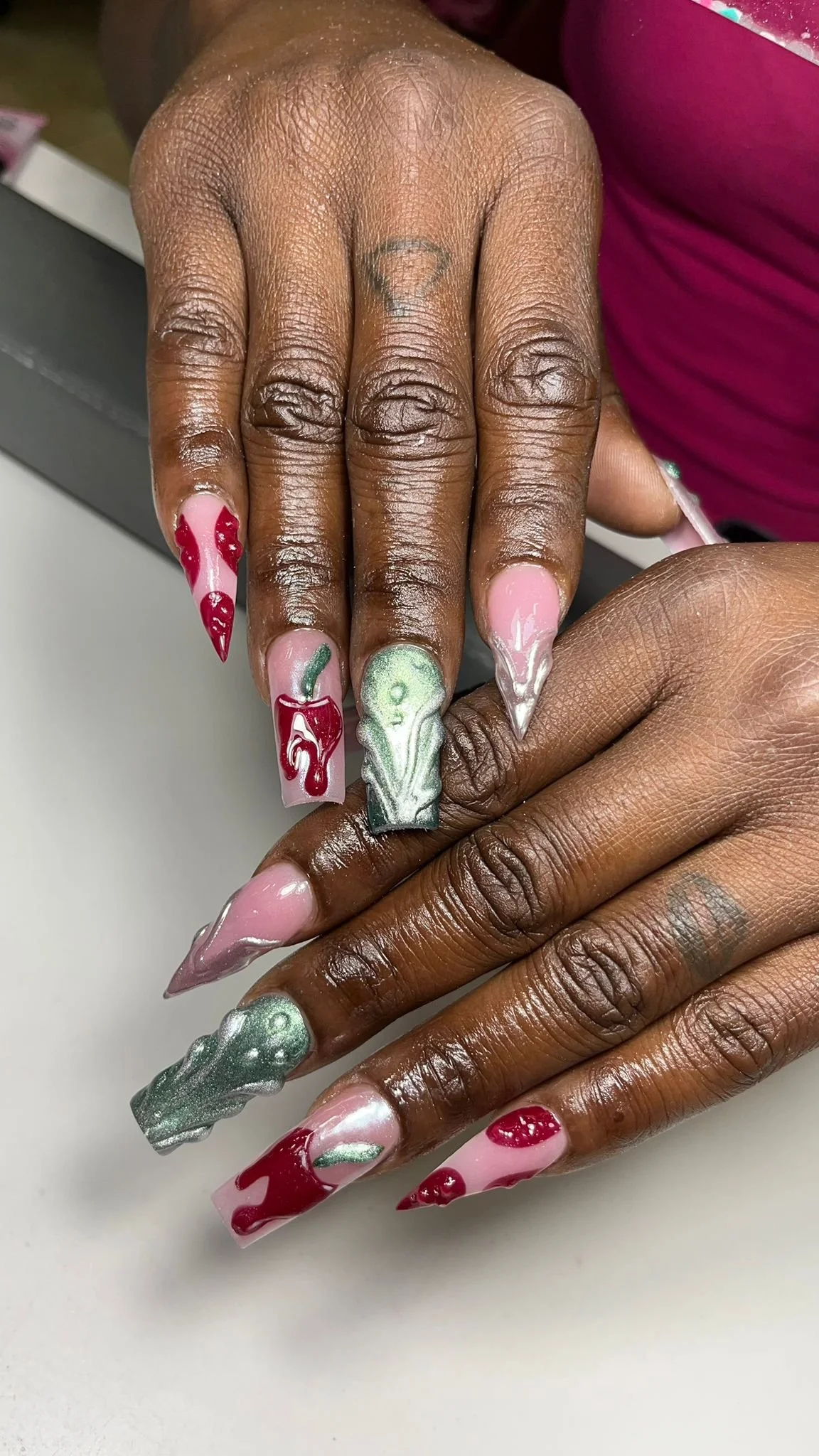 Woman's hand with elaborate Valentine's Day themed nail art, featuring pink, red, and silver designs resembling hearts, cherries, and abstract patterns.