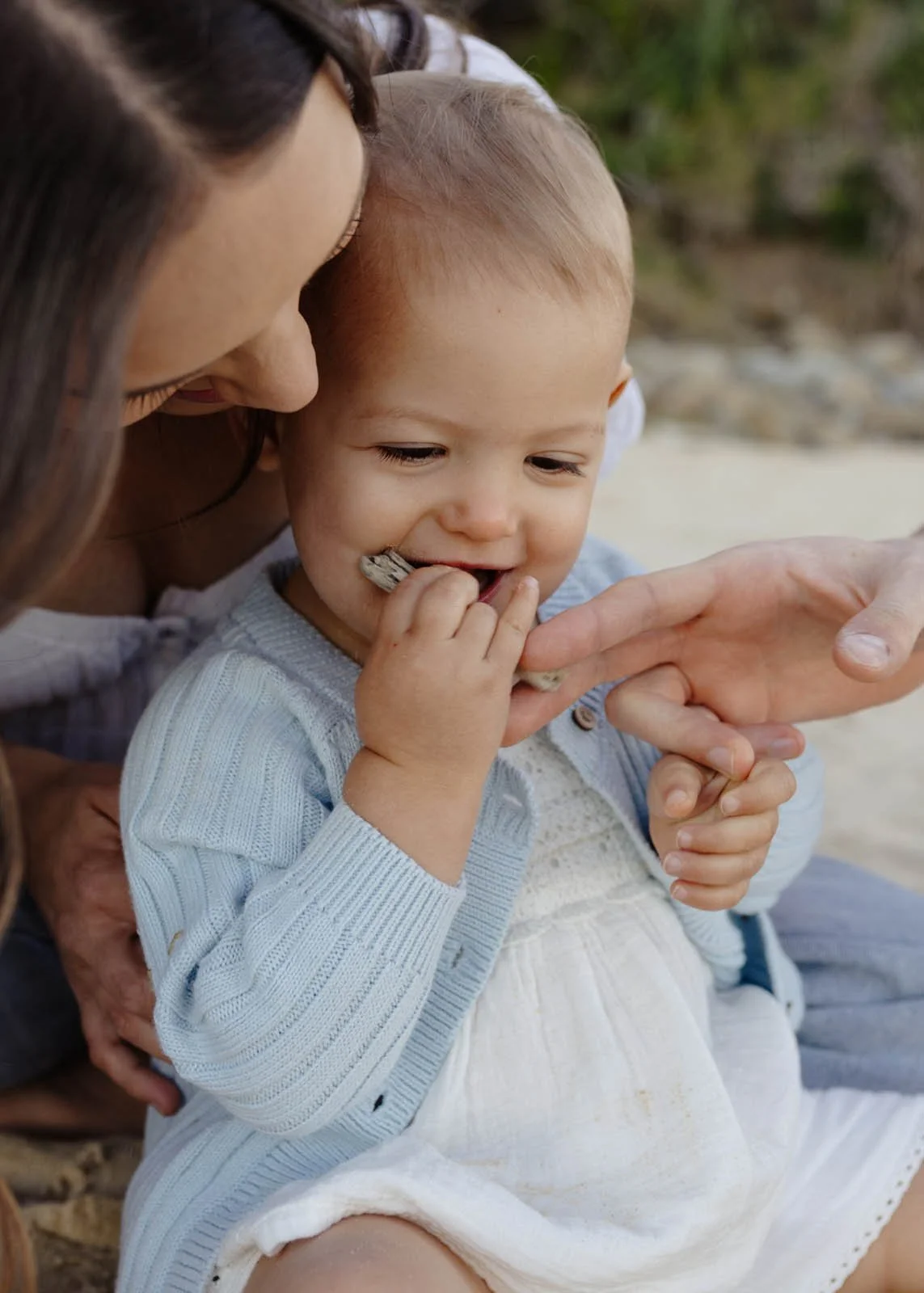 A woman and a toddler sitting outdoors, with the woman guiding the child's hand.