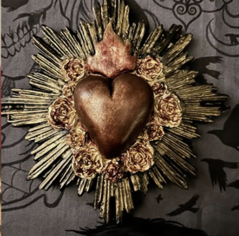 Decorative heart-shaped object surrounded by gold roses and metallic rays.