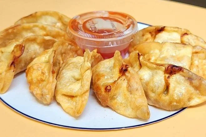 Plate of fried dumplings with a side of red dipping sauce in a small container