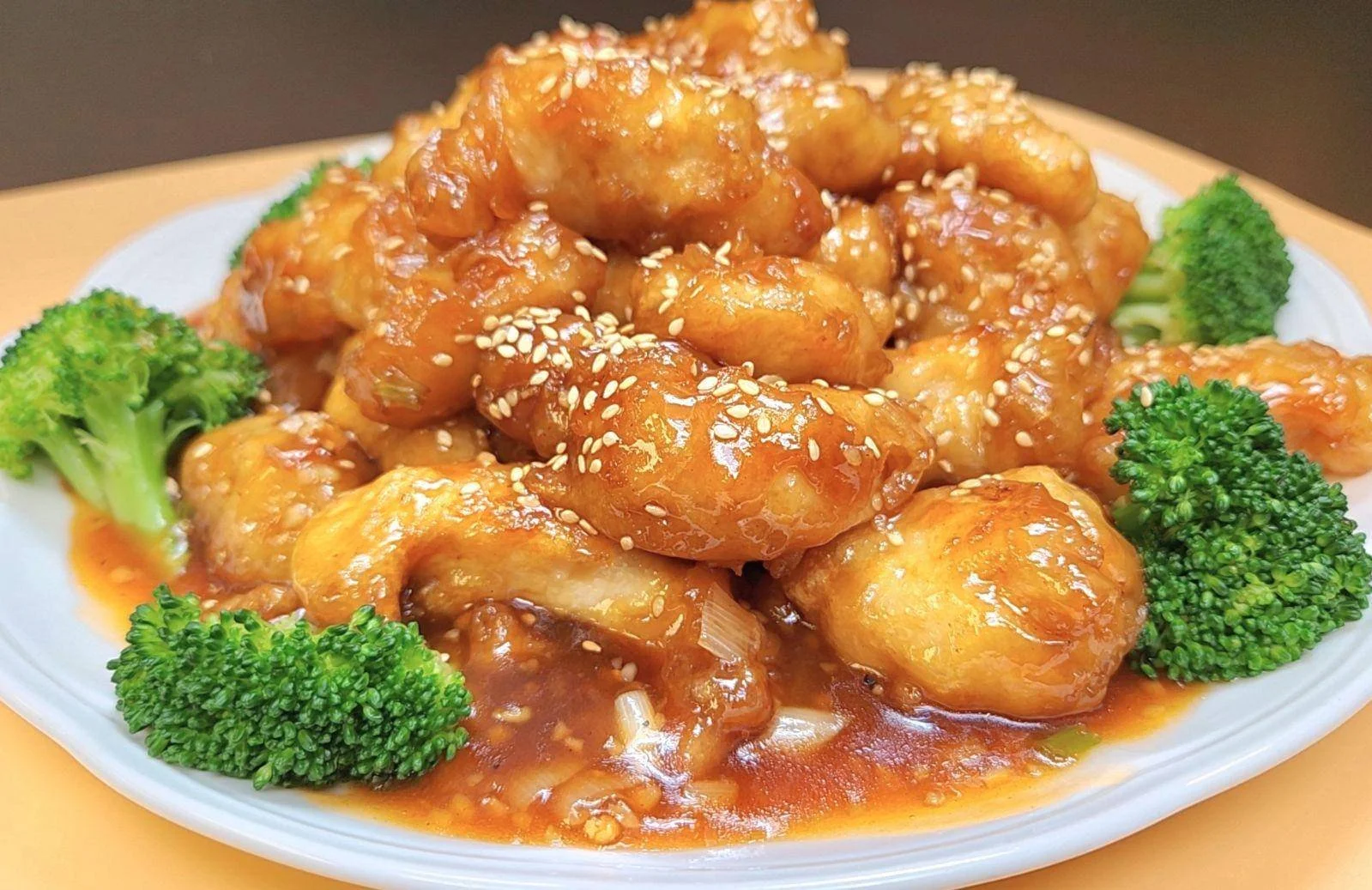 Plate of orange chicken with sesame seeds garnished with broccoli florets.