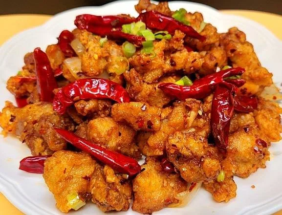 Plate of fried chicken pieces garnished with dried red chili peppers and chopped green onions.