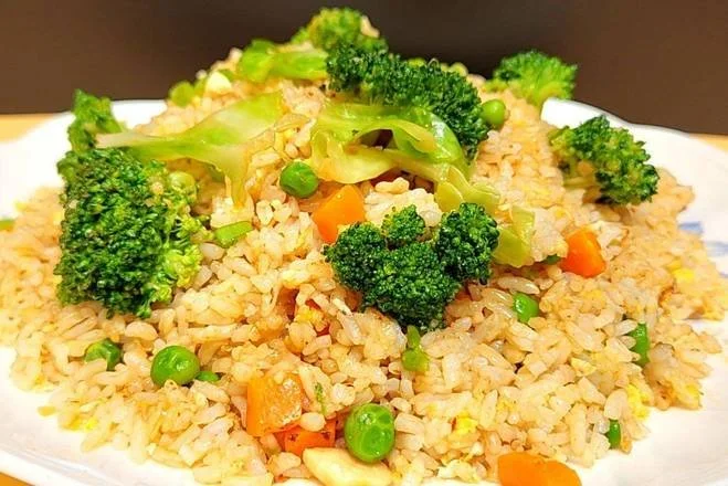 A plate of fried rice with broccoli, peas, and diced carrots garnished on top.
