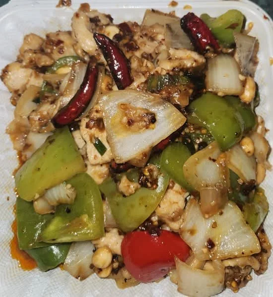 Stir-fried dish with chopped vegetables, dried red chili peppers, and ground meat in a takeout container.