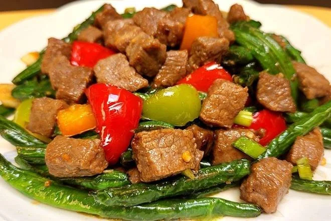 Stir-fried beef with bell peppers and green onions on a white plate.