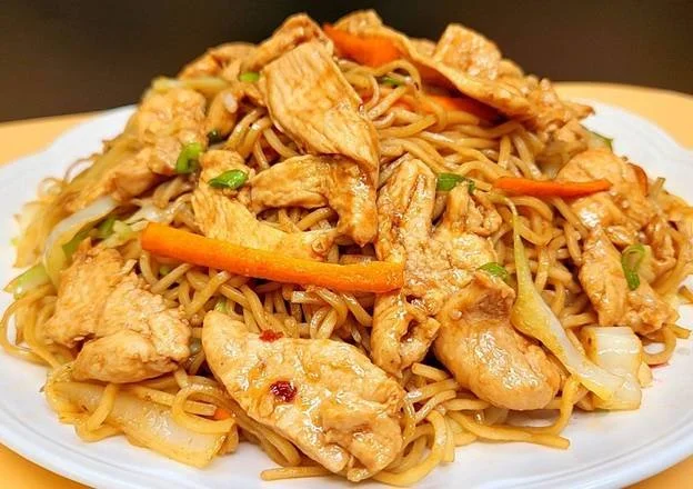 Plate of stir-fried chicken with noodles, vegetables, and sauce.