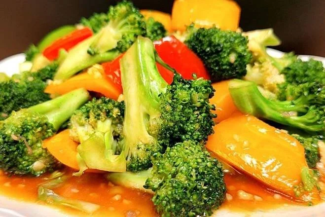 A plate of mixed steamed vegetables including broccoli, red bell peppers, yellow bell peppers, and green beans
