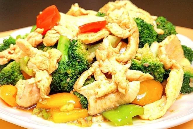 Stir-fried chicken with broccoli, peppers, and tomatoes on a white plate.