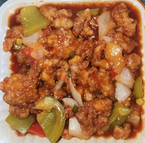 Sweet and sour chicken with green bell peppers, onions, and red peppers in a takeout container.