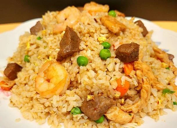 Fried rice with shrimp, beef cubes, peas, carrots, and egg on a white plate.