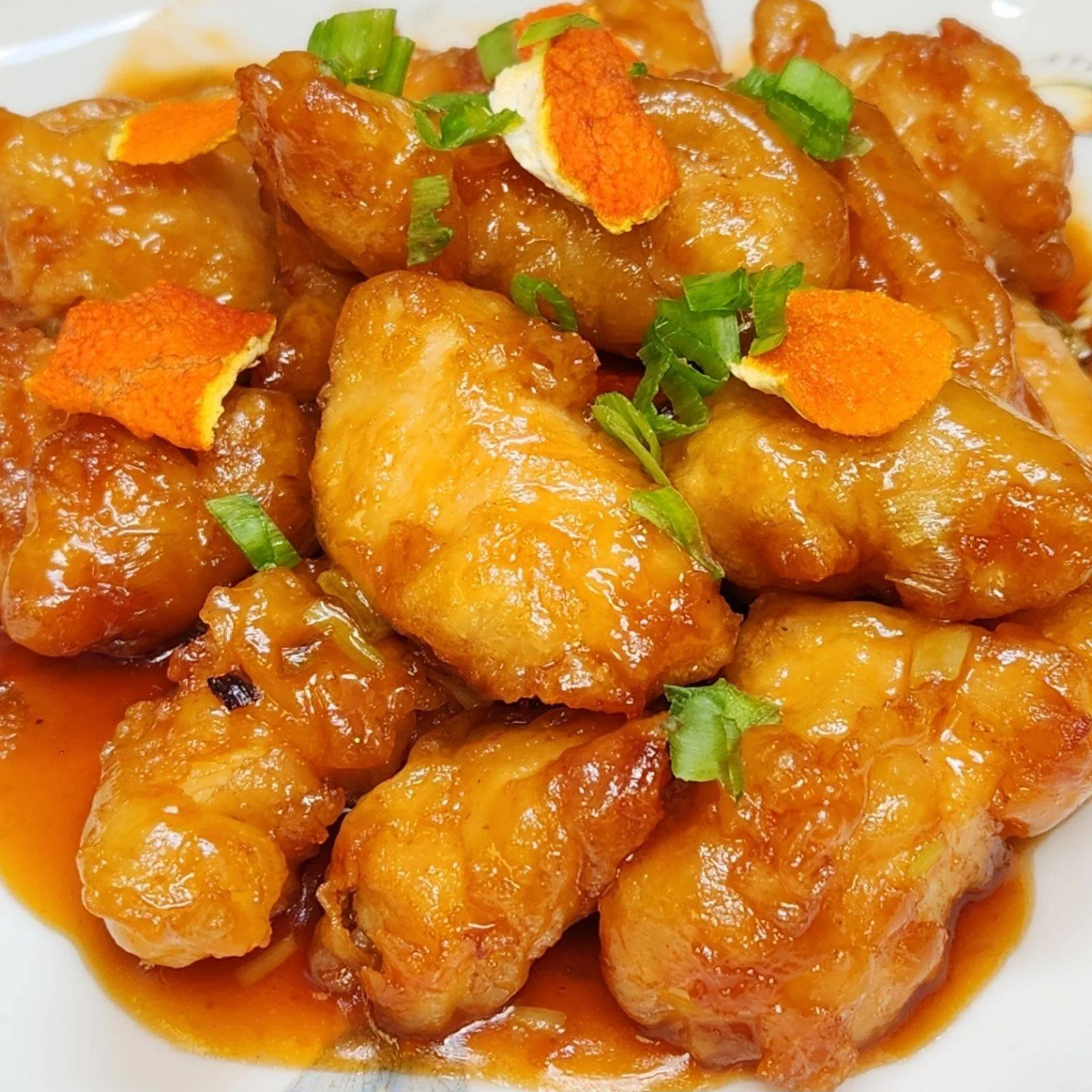 Plate of sweet and sour chicken garnished with green onions and orange peel.