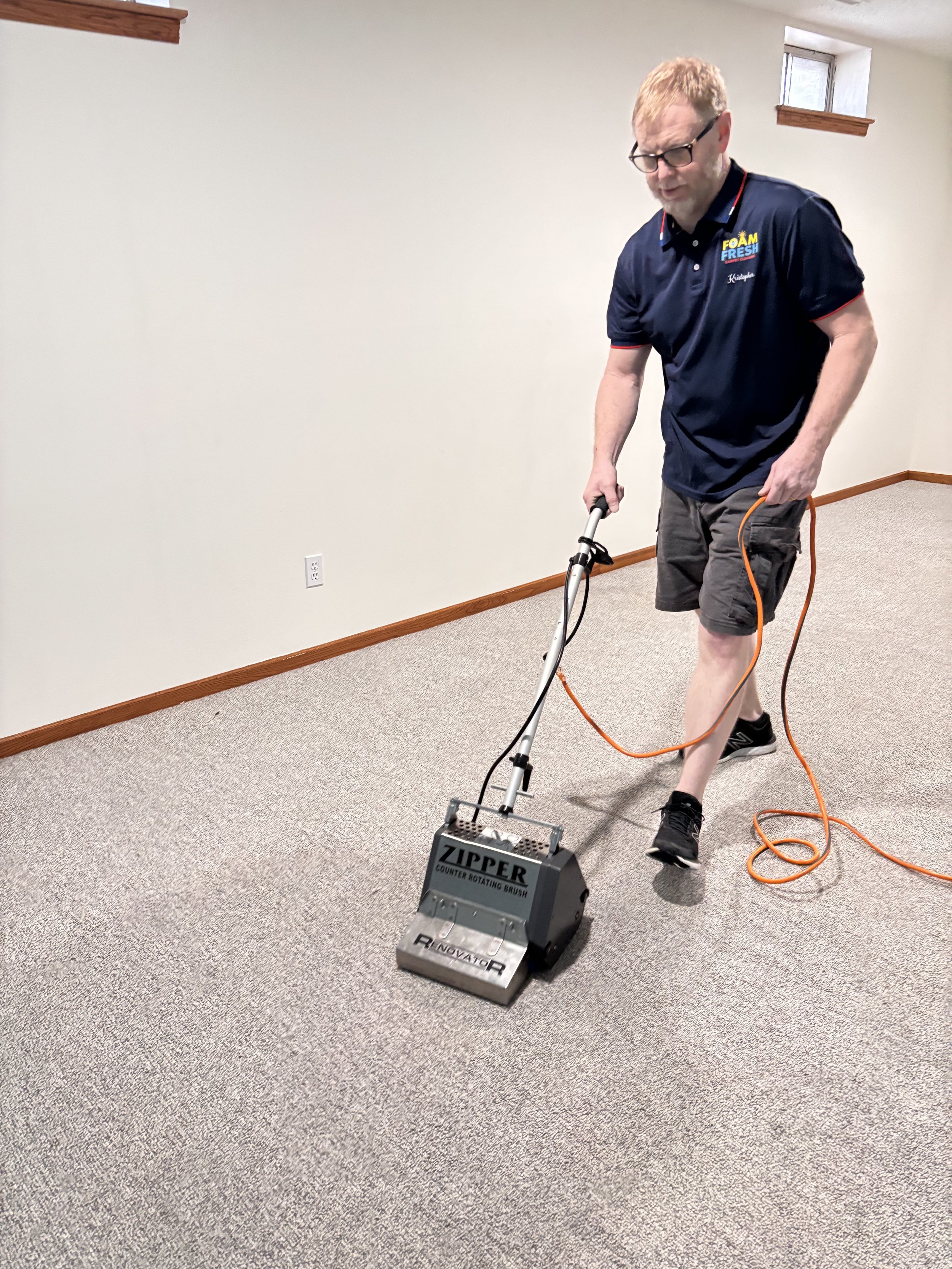 Man using a Zipper Counter Rotating Brush on a carpeted floor in a room with beige walls and small windows.