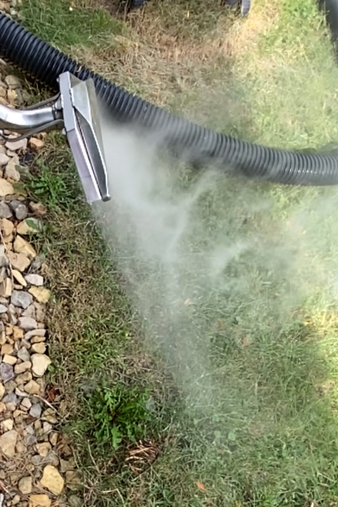 A pressure washer spraying water onto grass and gravel outdoors.