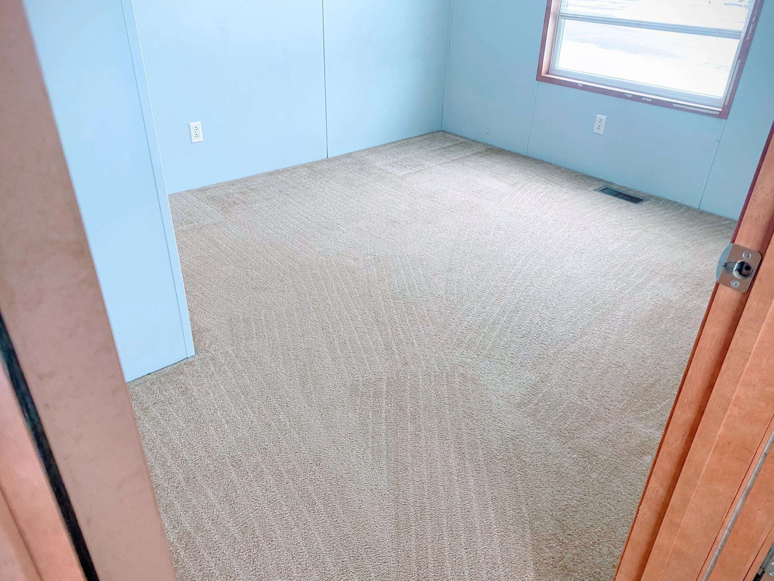 Empty room with light blue walls, beige carpet, and a window with blinds.