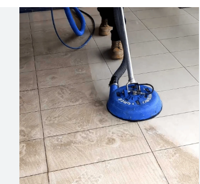 A floor cleaning machine with a blue base and hose, cleaning tiled floor.