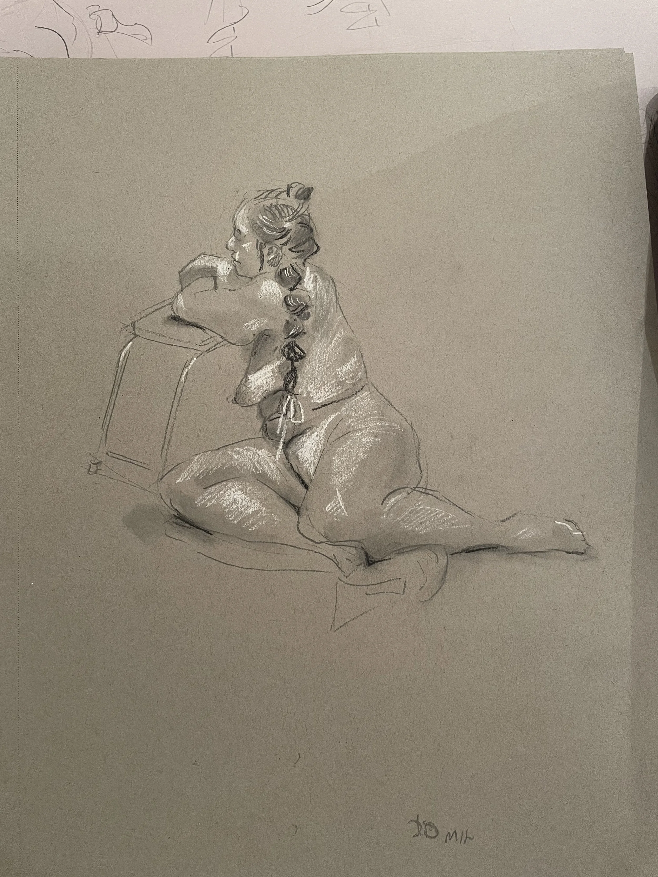 A detailed pencil sketch of a woman sitting kneeling on the ground, resting her arms on a small table, with her head turned to the side and long hair styled in loose curls, on textured paper.