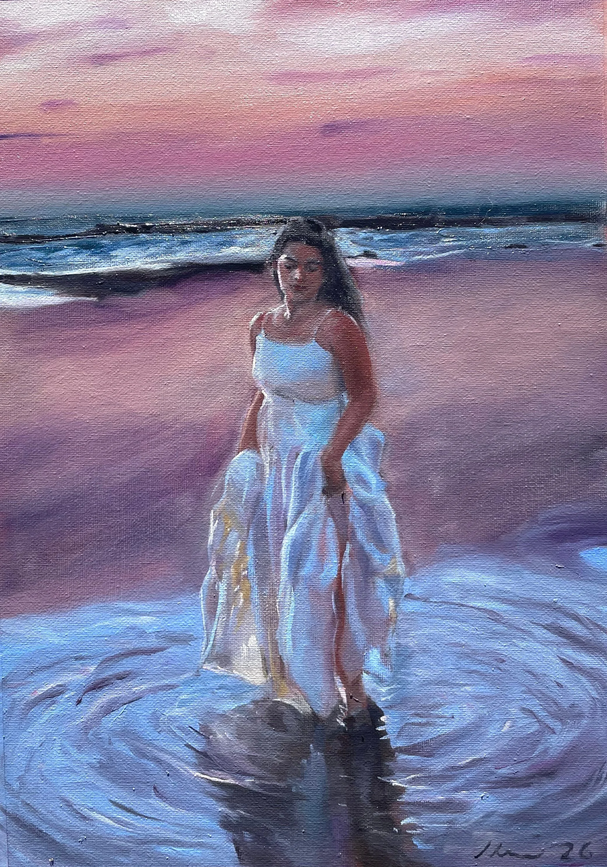A woman in a white dress standing in the shallow water at the beach during sunset.