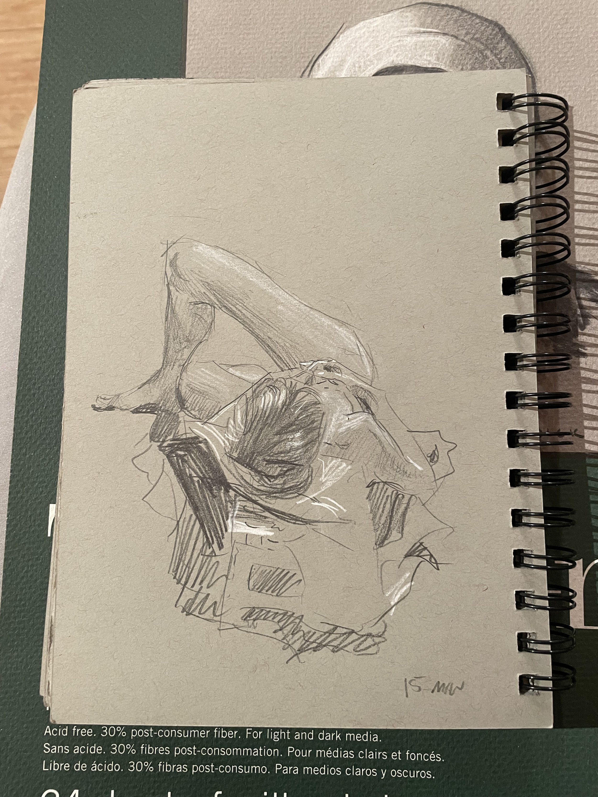 Pencil sketch of a woman sitting on a cloth, with one arm resting on her knee and her head tilted back, drawn on a spiral-notebook page.