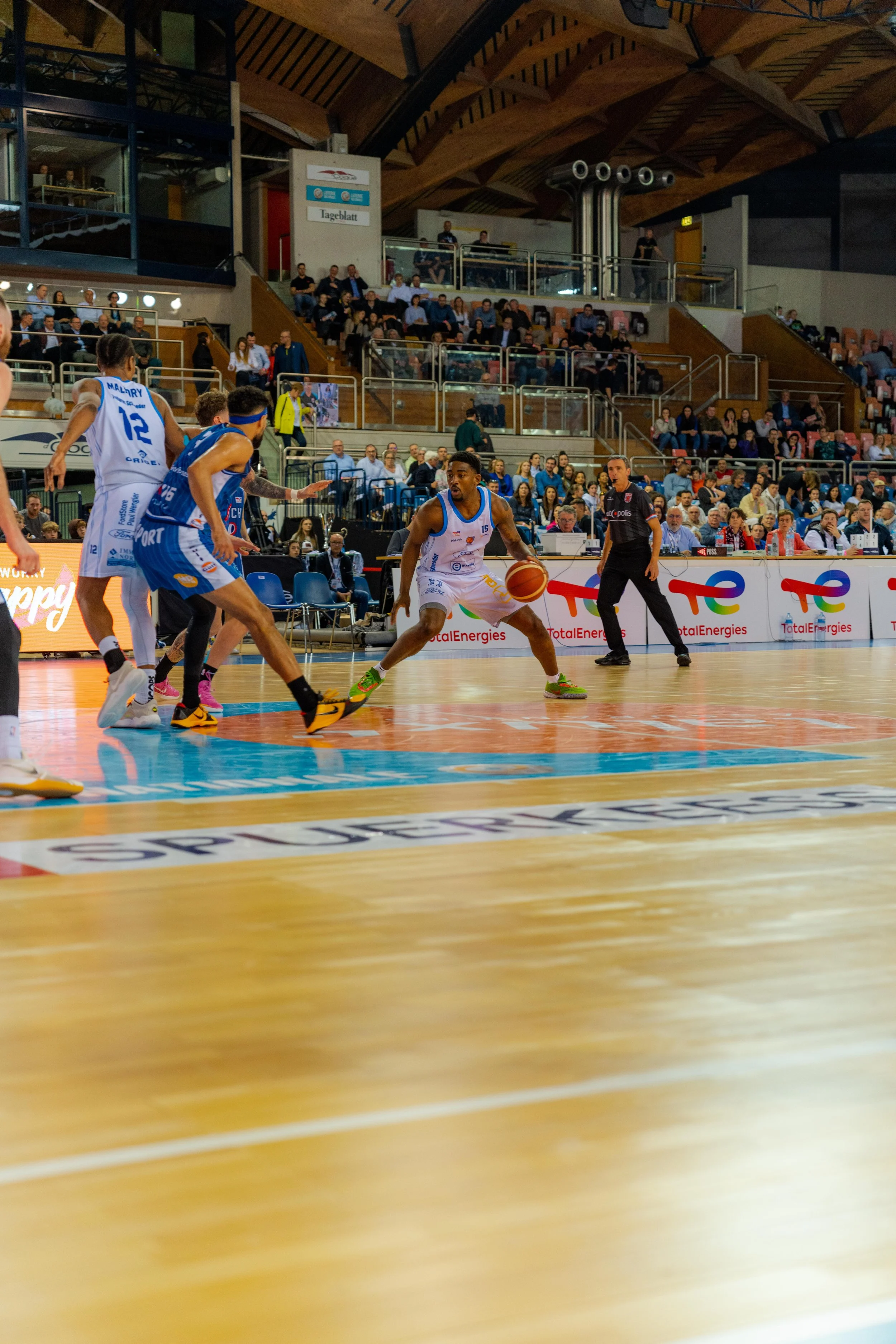 A basketball game in progress with players on the court and spectators in the stands.