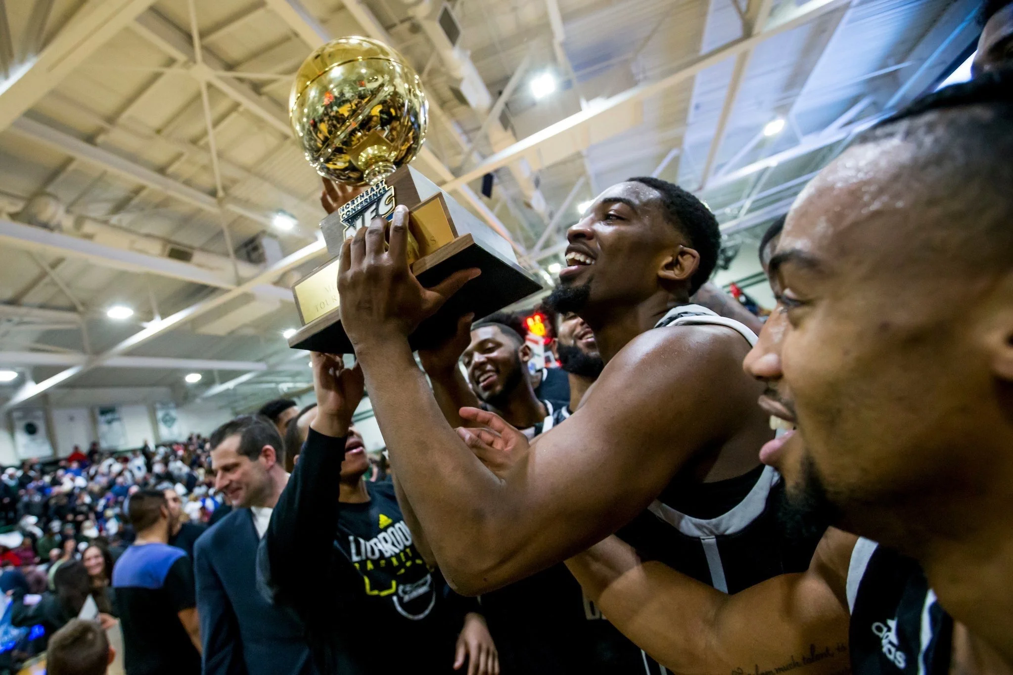 A basketball team celebrates as a player holds up a trophy in a gymnasium. The team is smiling and appears joyful.