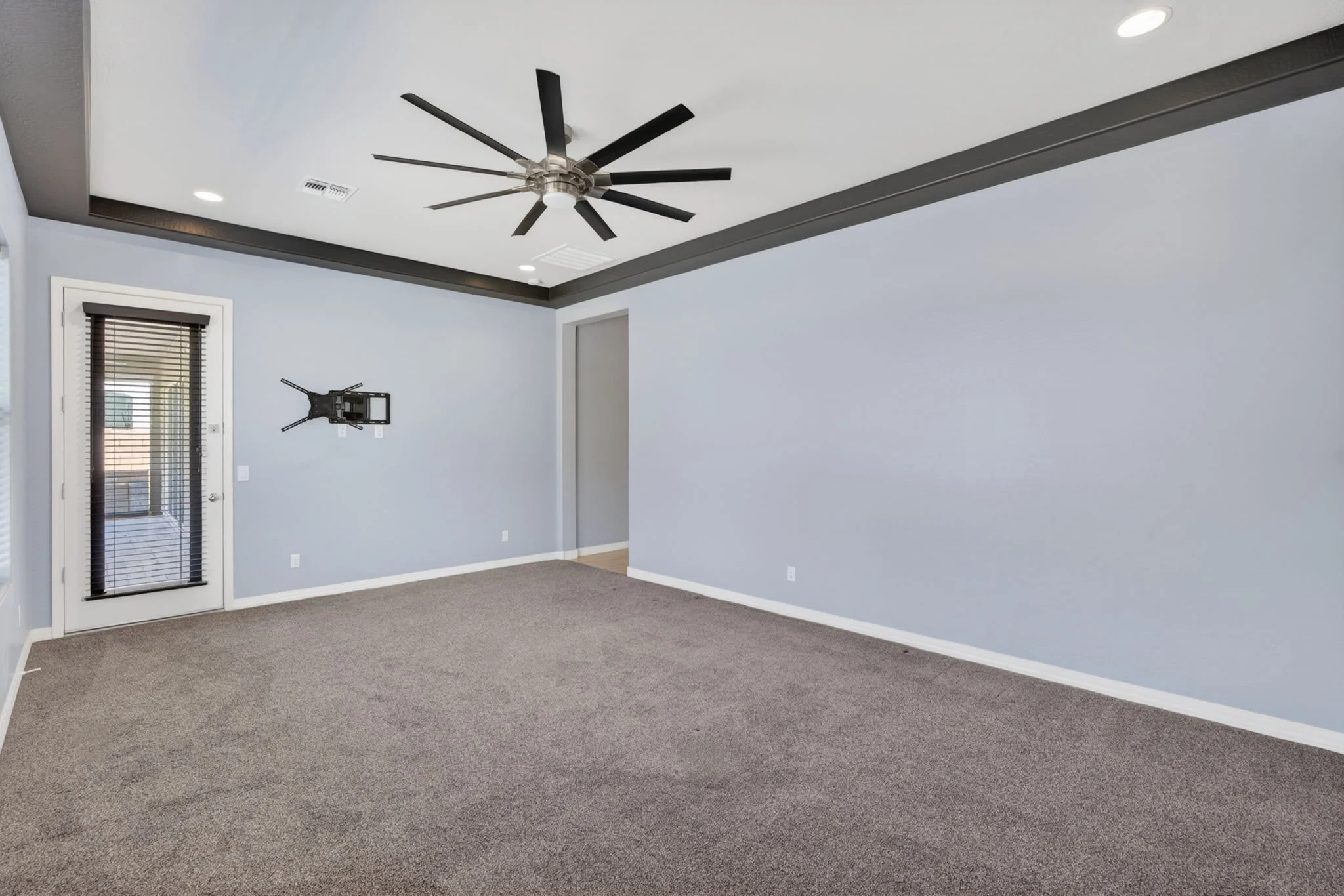 Empty living room with grey walls, brown carpet, and a ceiling fan.