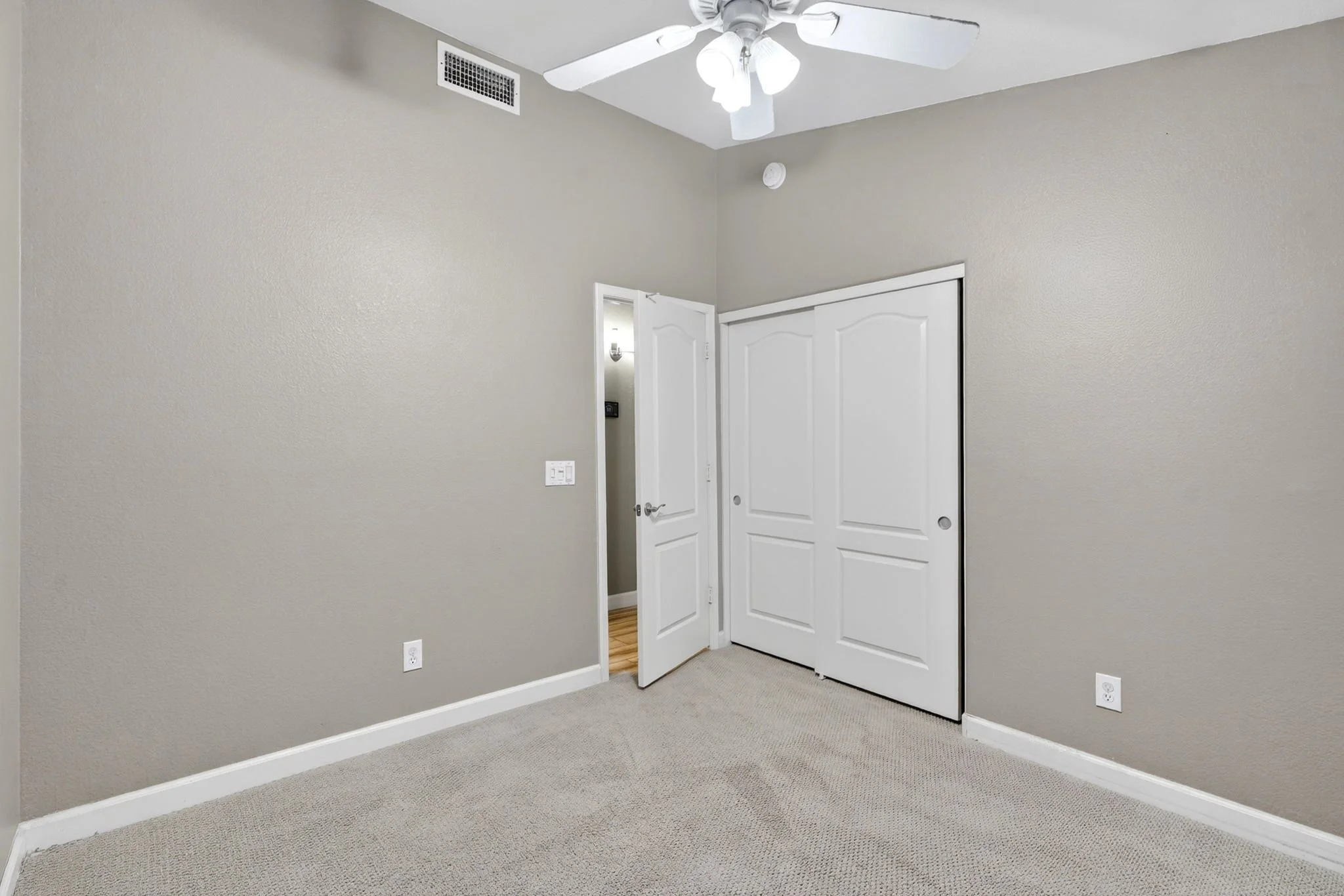 Empty room with beige walls, white closet doors, ceiling fan with light, and carpeted floor.