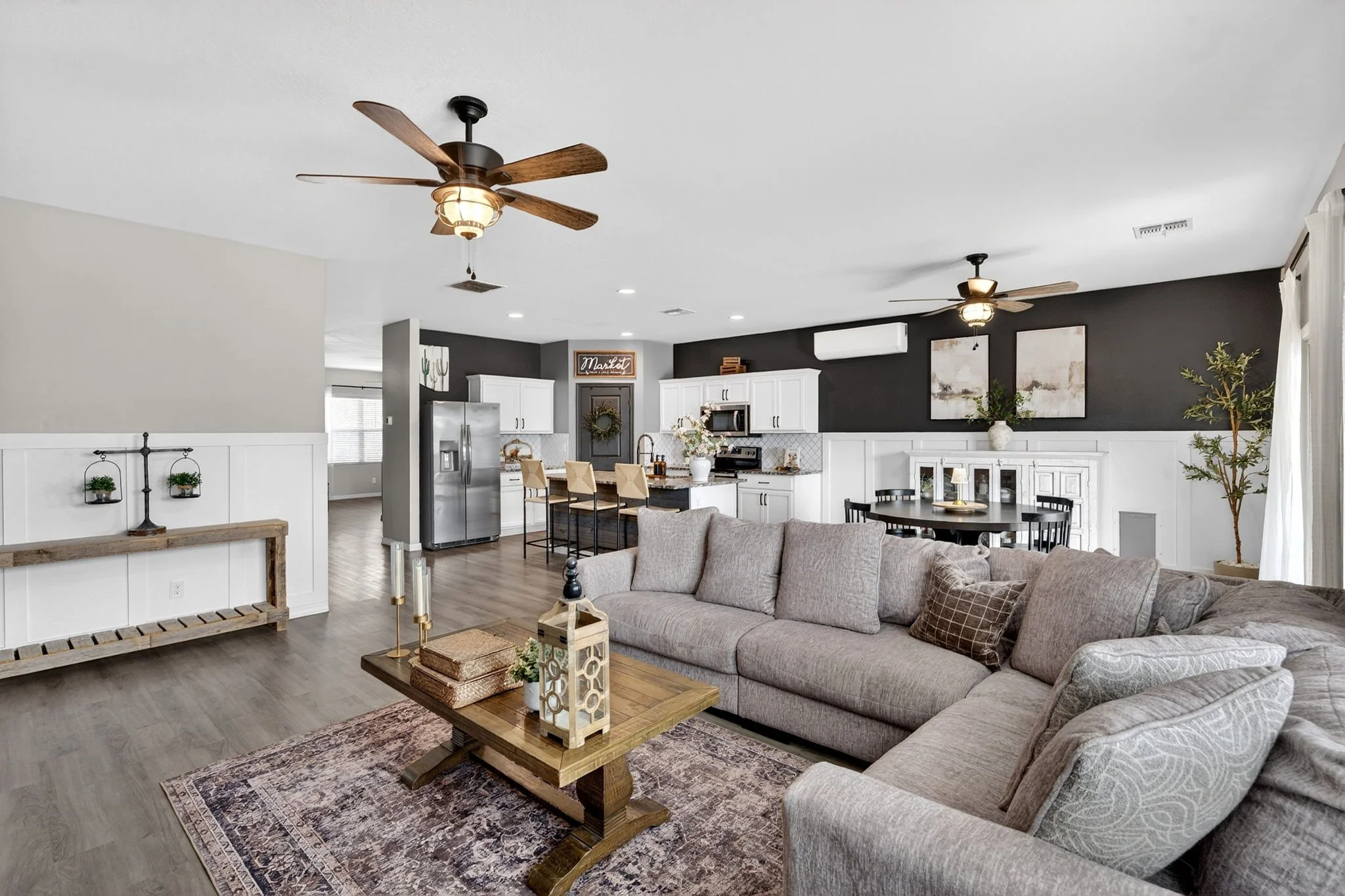 Open-concept living room and kitchen with ceiling fans, gray and white walls, and modern decor.
