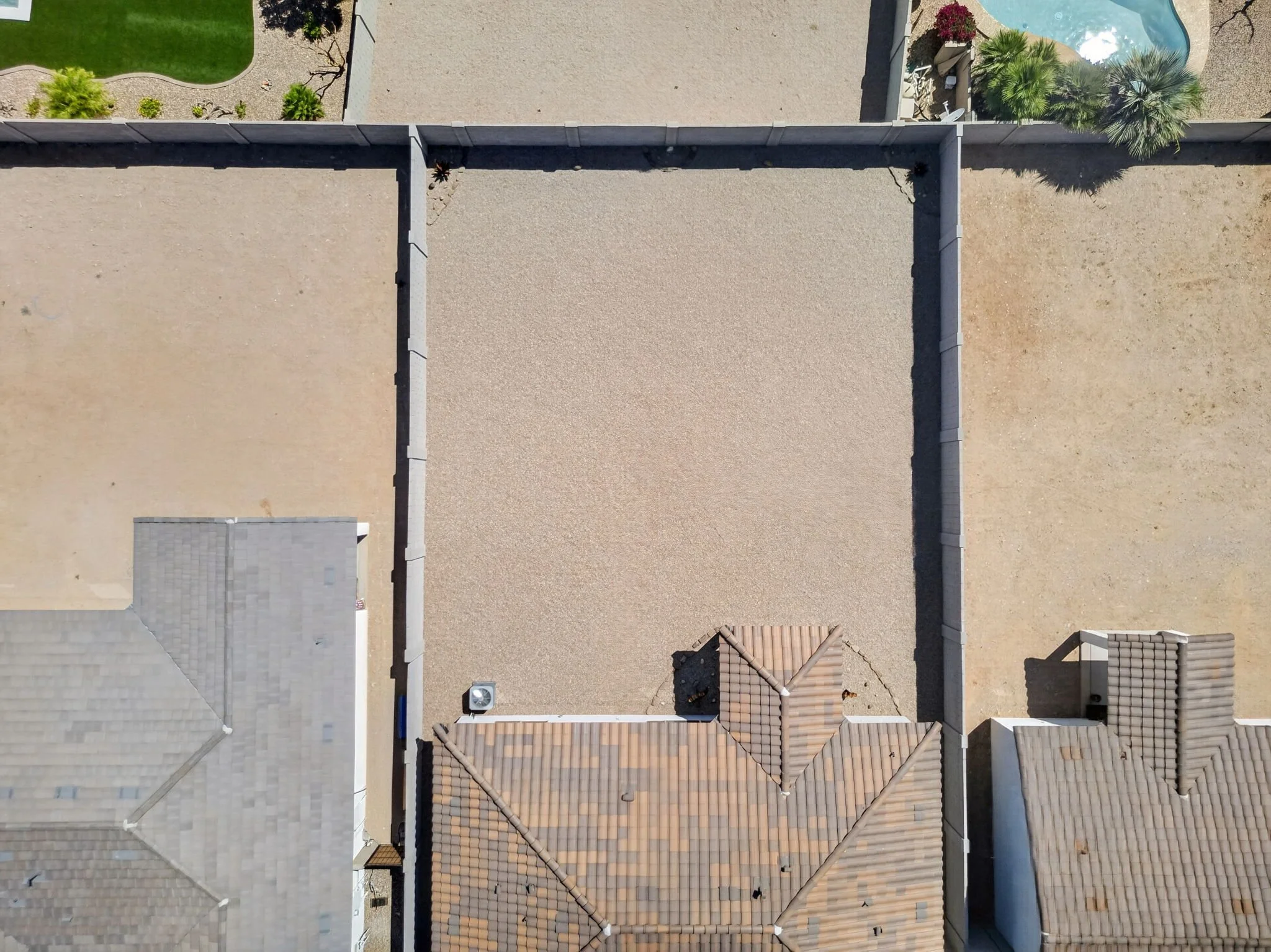 An aerial view of residential rooftops, yards, and a swimming pool with palm trees.