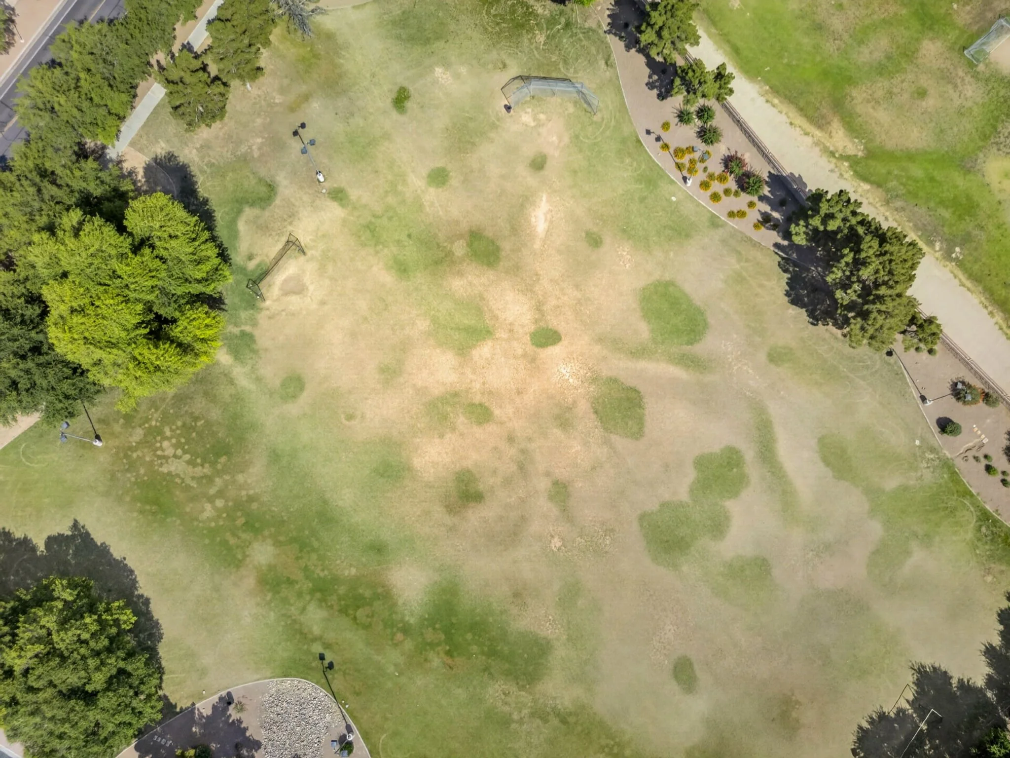 An aerial view of a park with open grassy areas, trees lining the perimeter, walking paths, and small structures such as benches and gazebos.