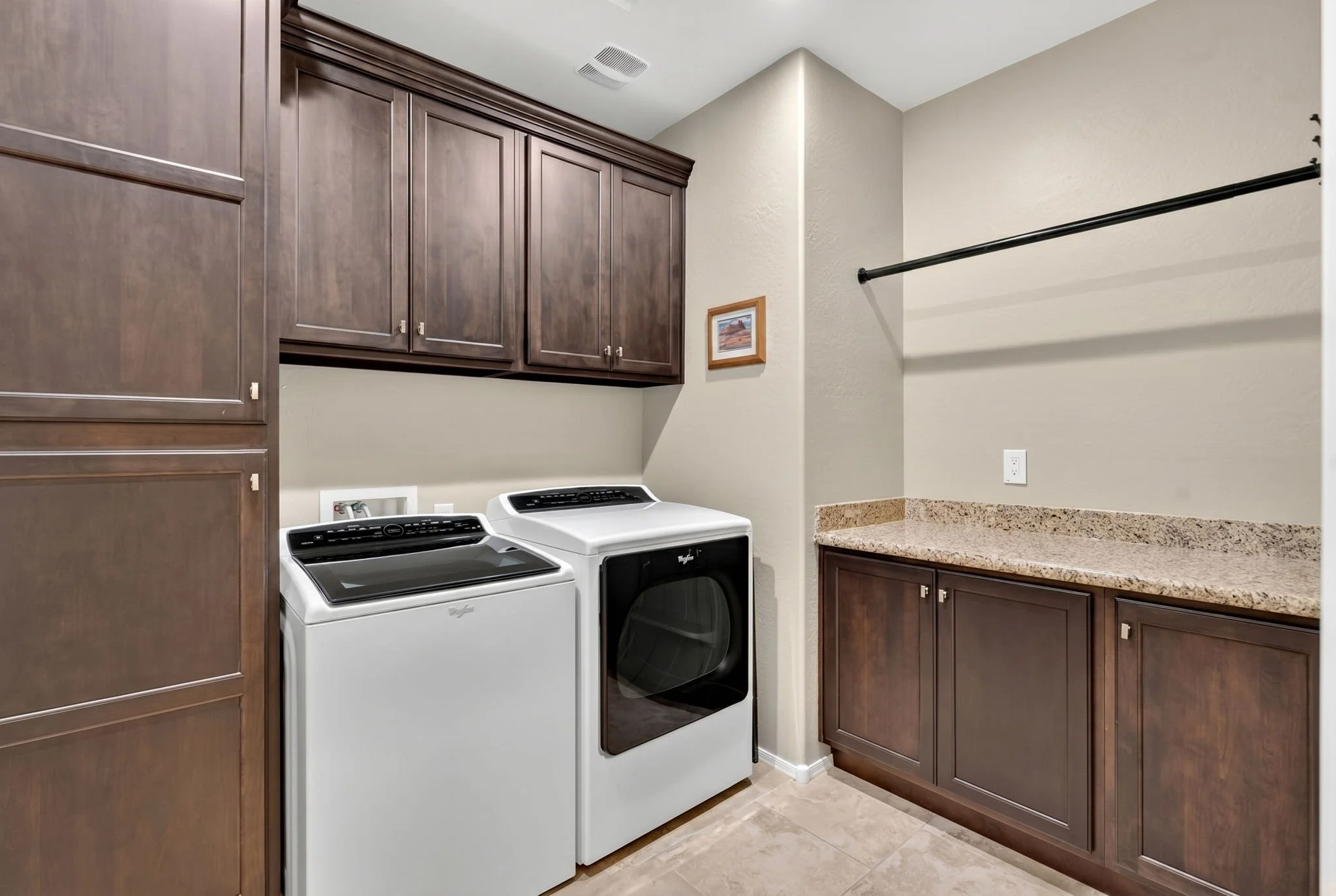 Laundry room with dark wooden cabinets, a white washing machine, a white dryer, granite countertops, and a wall-mounted picture frame.