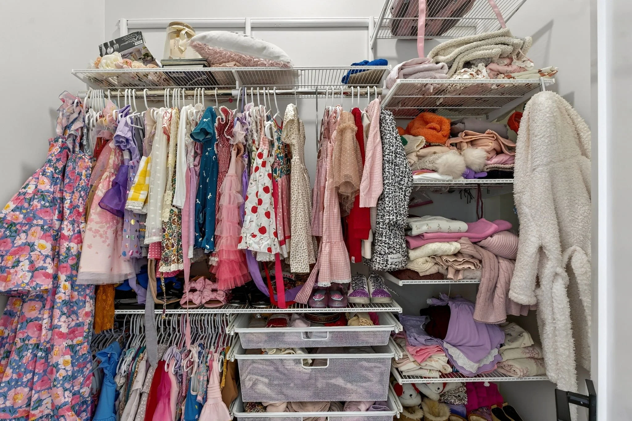 A closet with organized shelves and hanging rods filled with children’s clothing, shoes, and accessories.