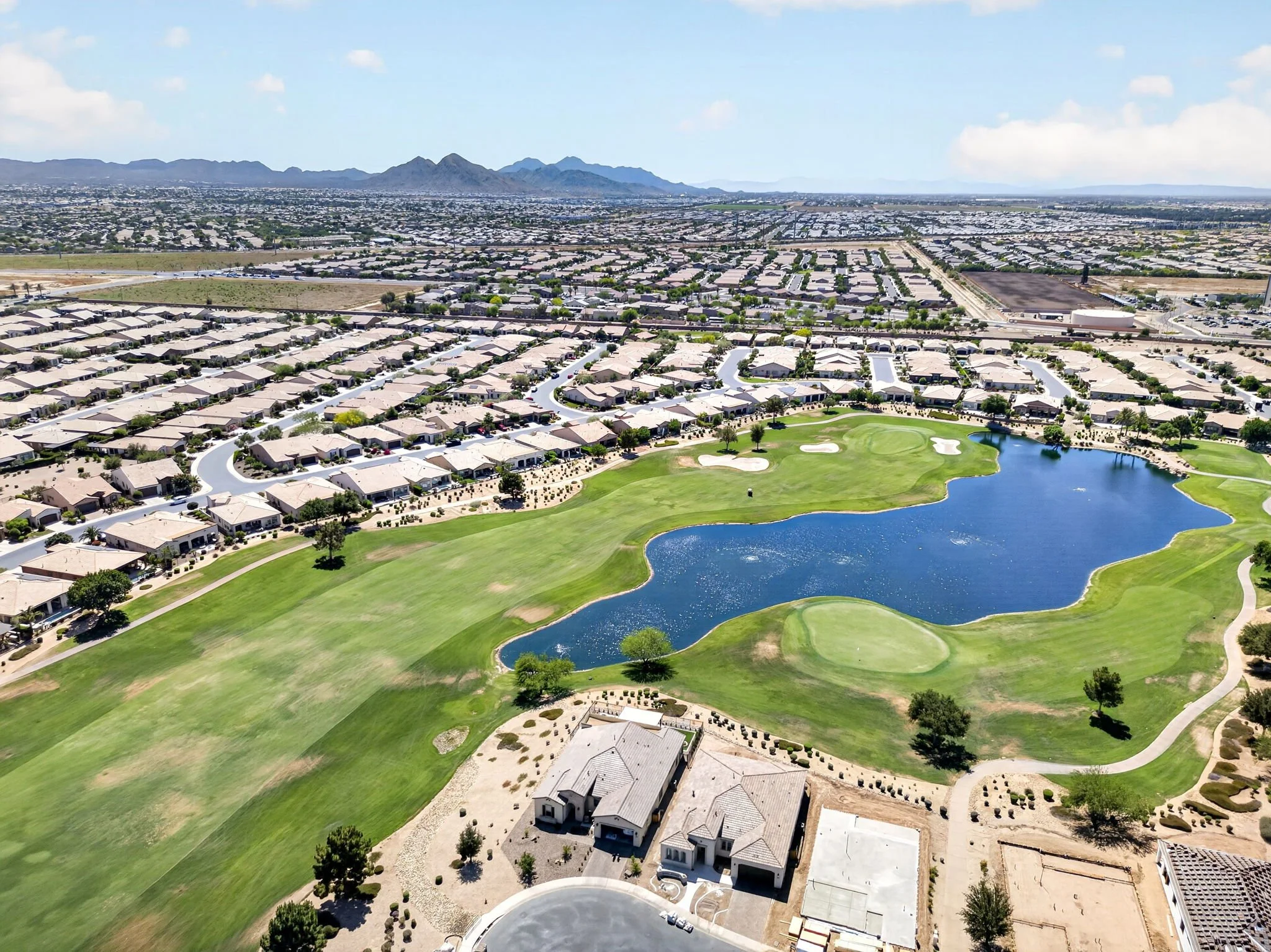 Aerial view of a suburban neighborhood near a golf course with a small pond and mountains in the distance.