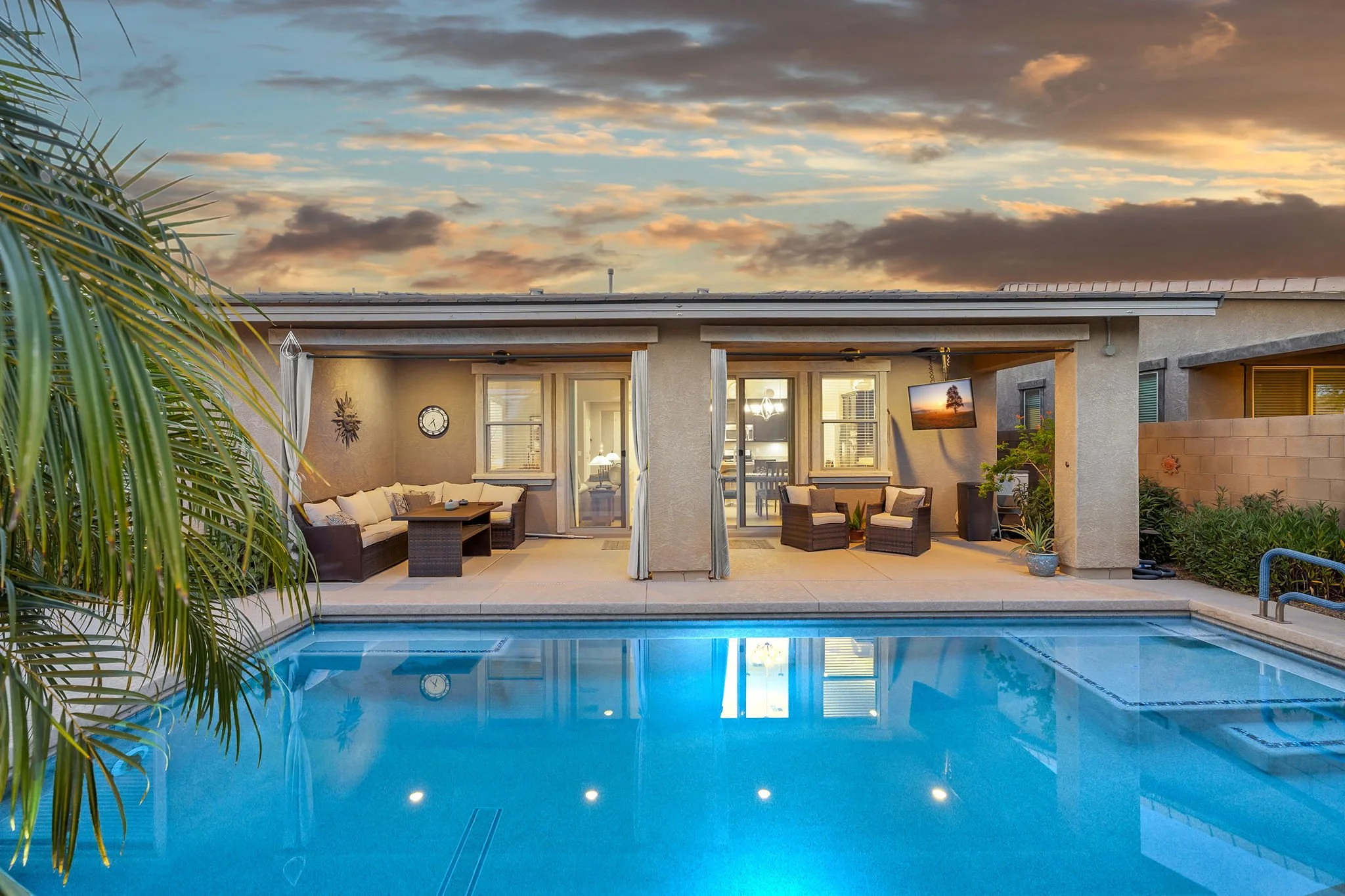 Backyard view of a house with an outdoor patio, swimming pool, and sunset sky.