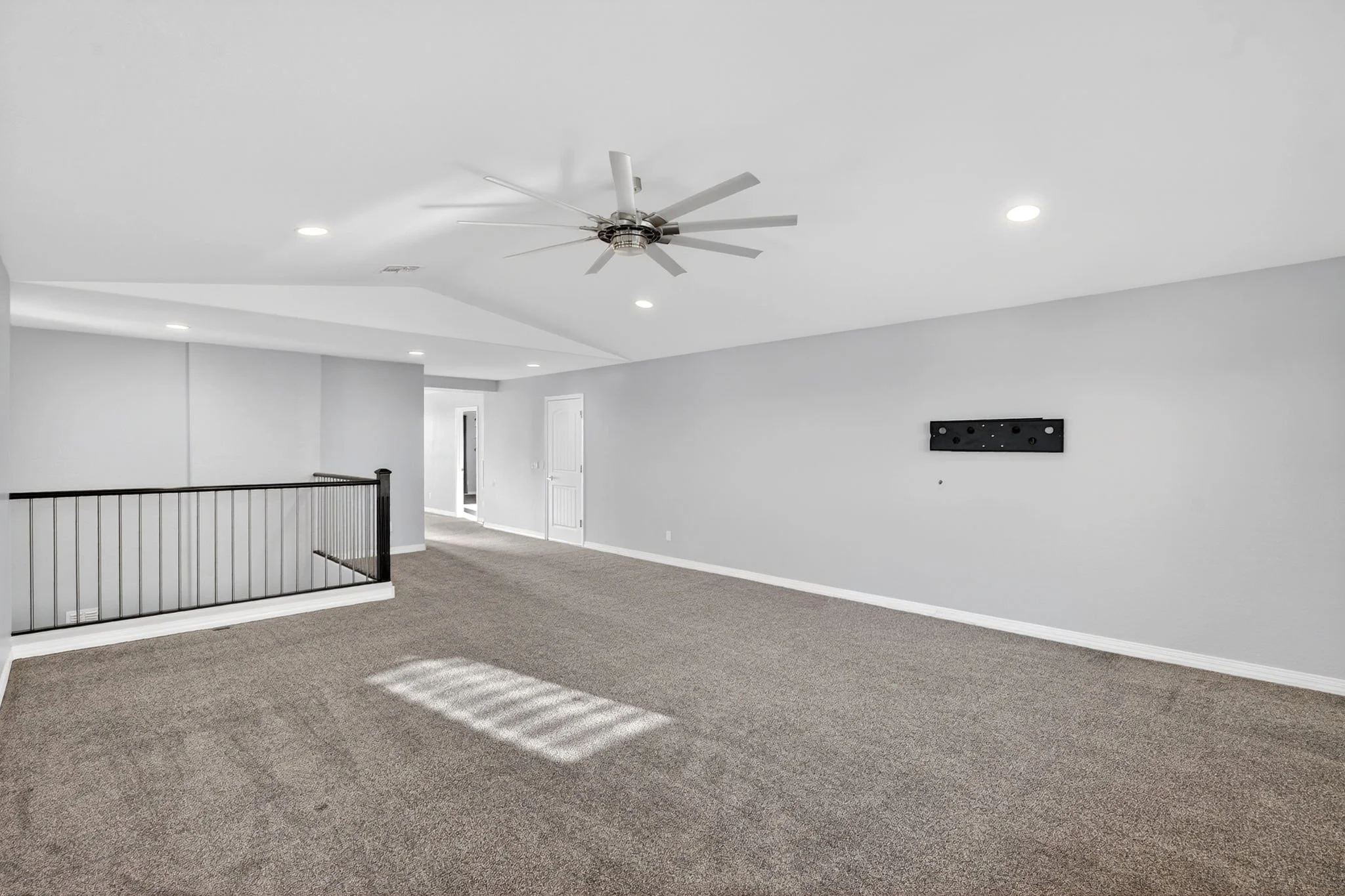 Empty living room with beige carpet, white walls, and a ceiling fan with lights.