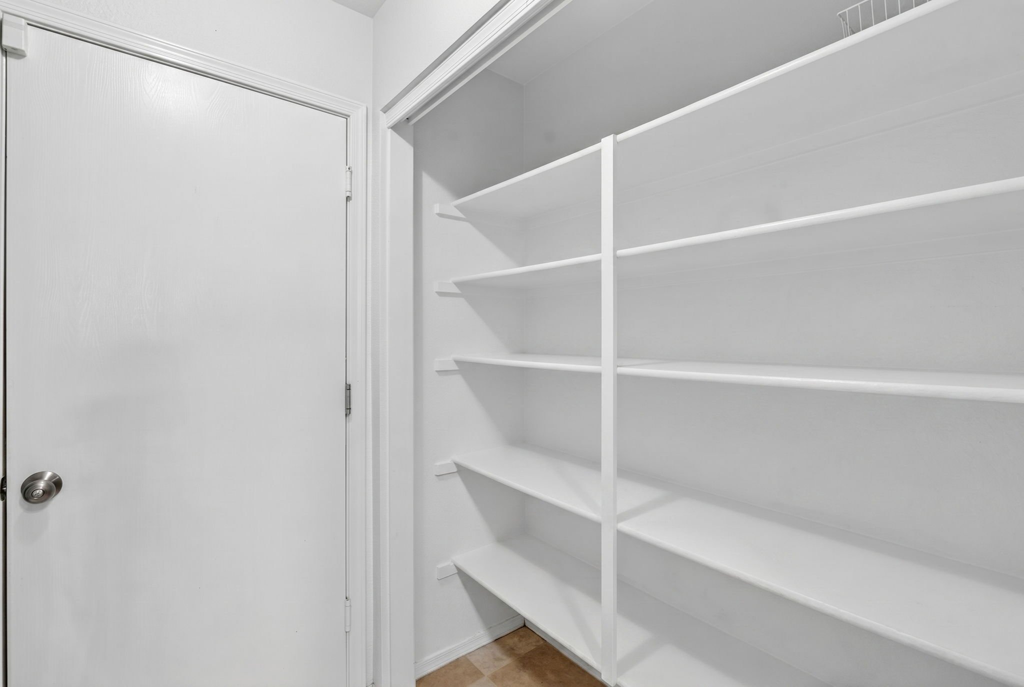 Empty white closet with multiple shelves, white door with a doorknob, and light brown wooden floor.