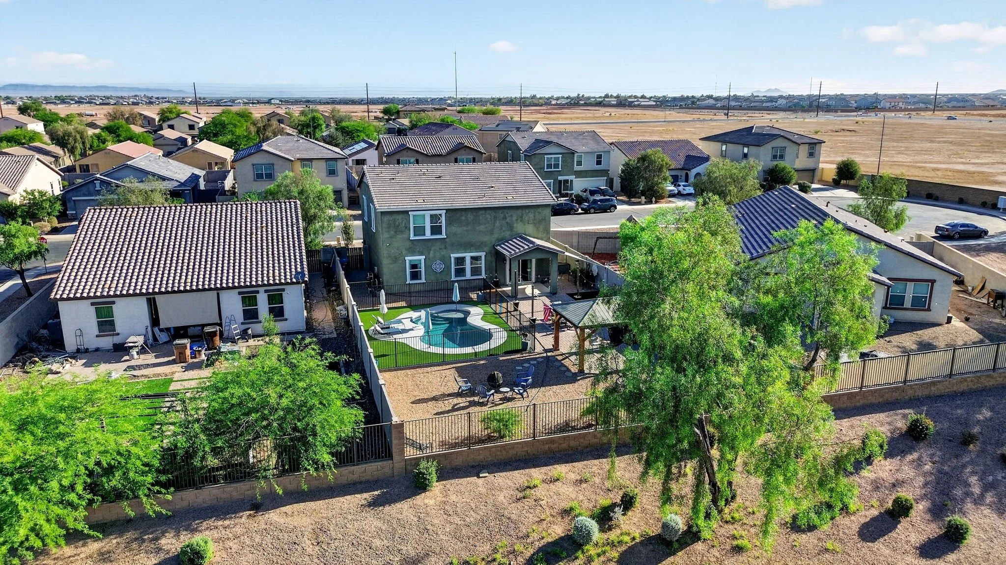 Aerial view of a suburban neighborhood with houses, trees, and a backyard with a swimming pool and patio furniture.
