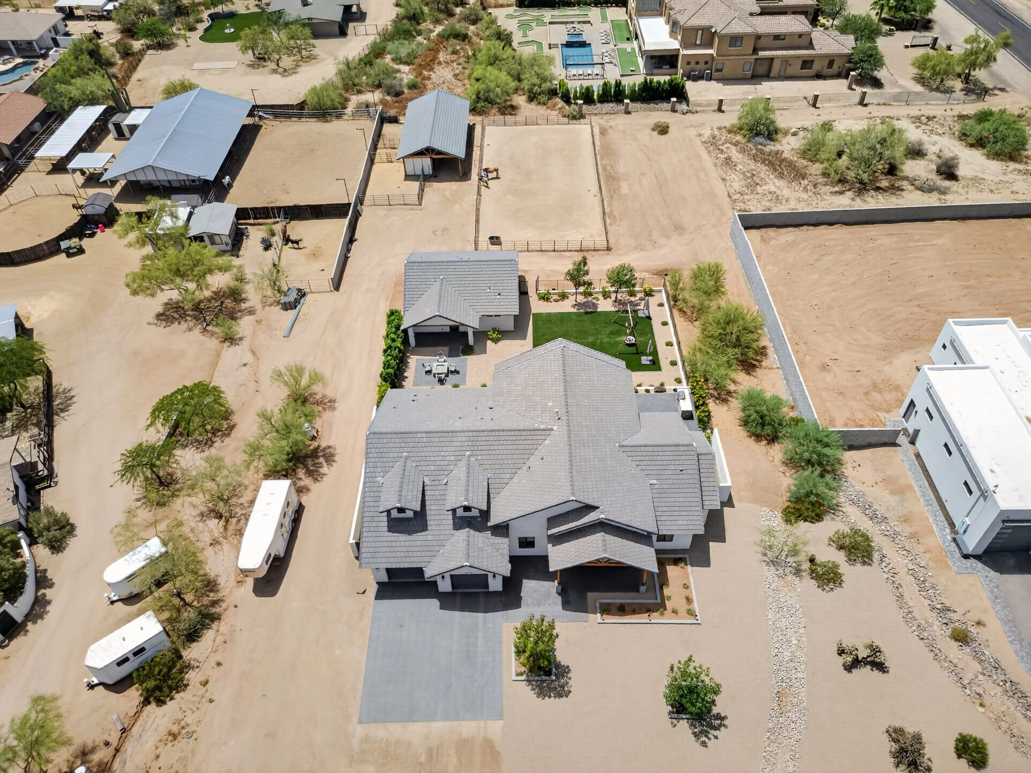 An aerial view of a residential area with houses, trees, and open lots, some fenced, in a dry, desert-like environment.