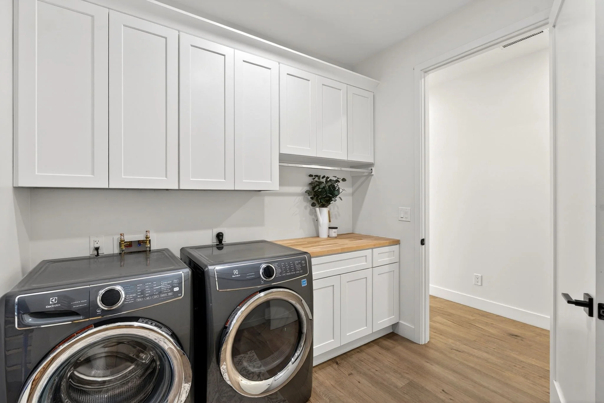 A modern laundry room with white cabinets, a wooden countertop, and a pair of black front-loading Electrolux washing machines.