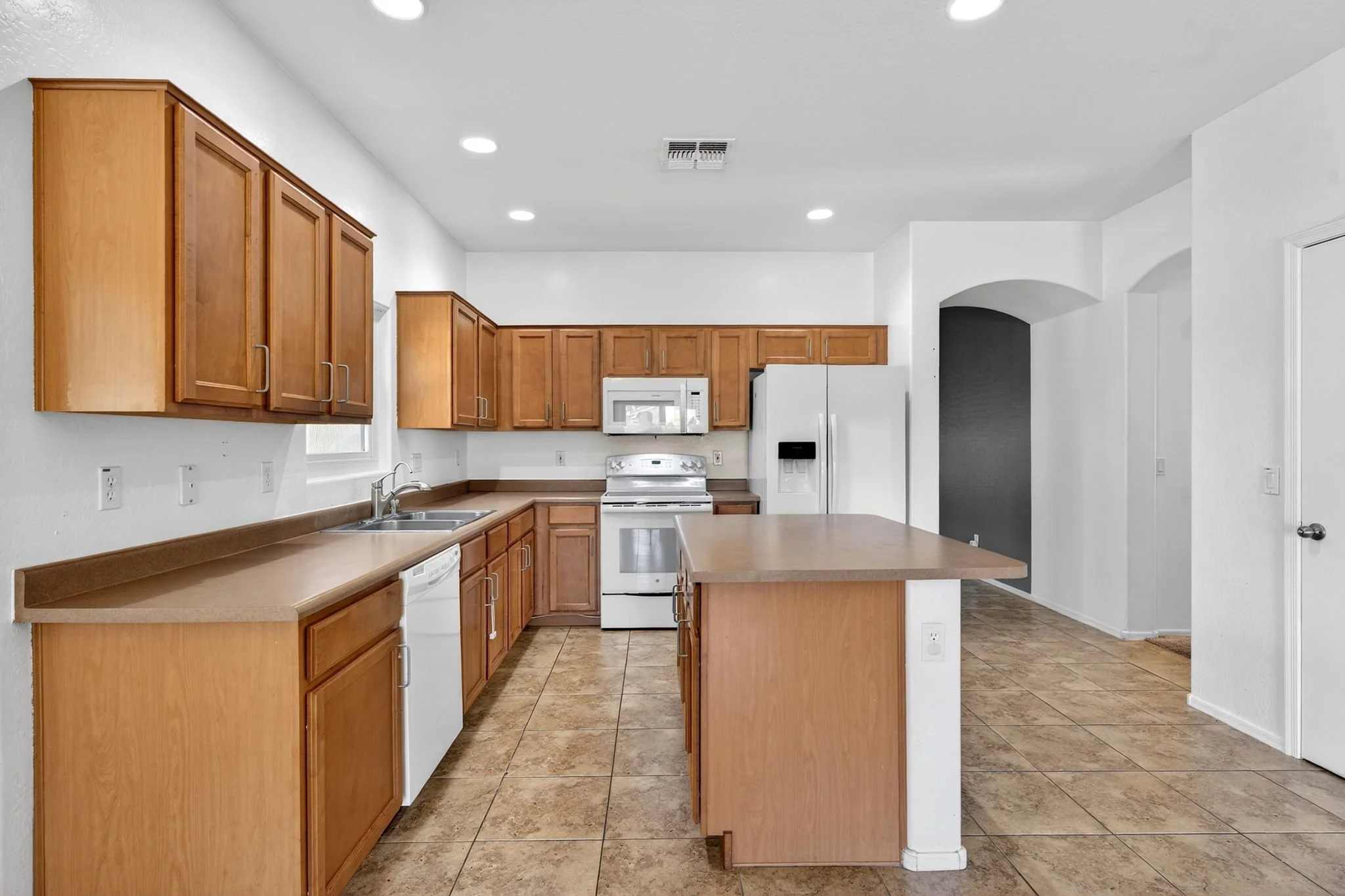 Kitchen with wooden cabinets, white appliances, and tiled floor.