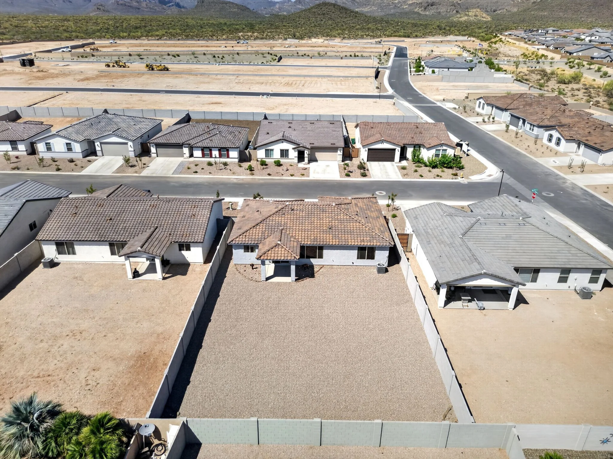  aerial view of a suburban neighborhood with houses, some under construction, in a desert landscape with mountains in the background