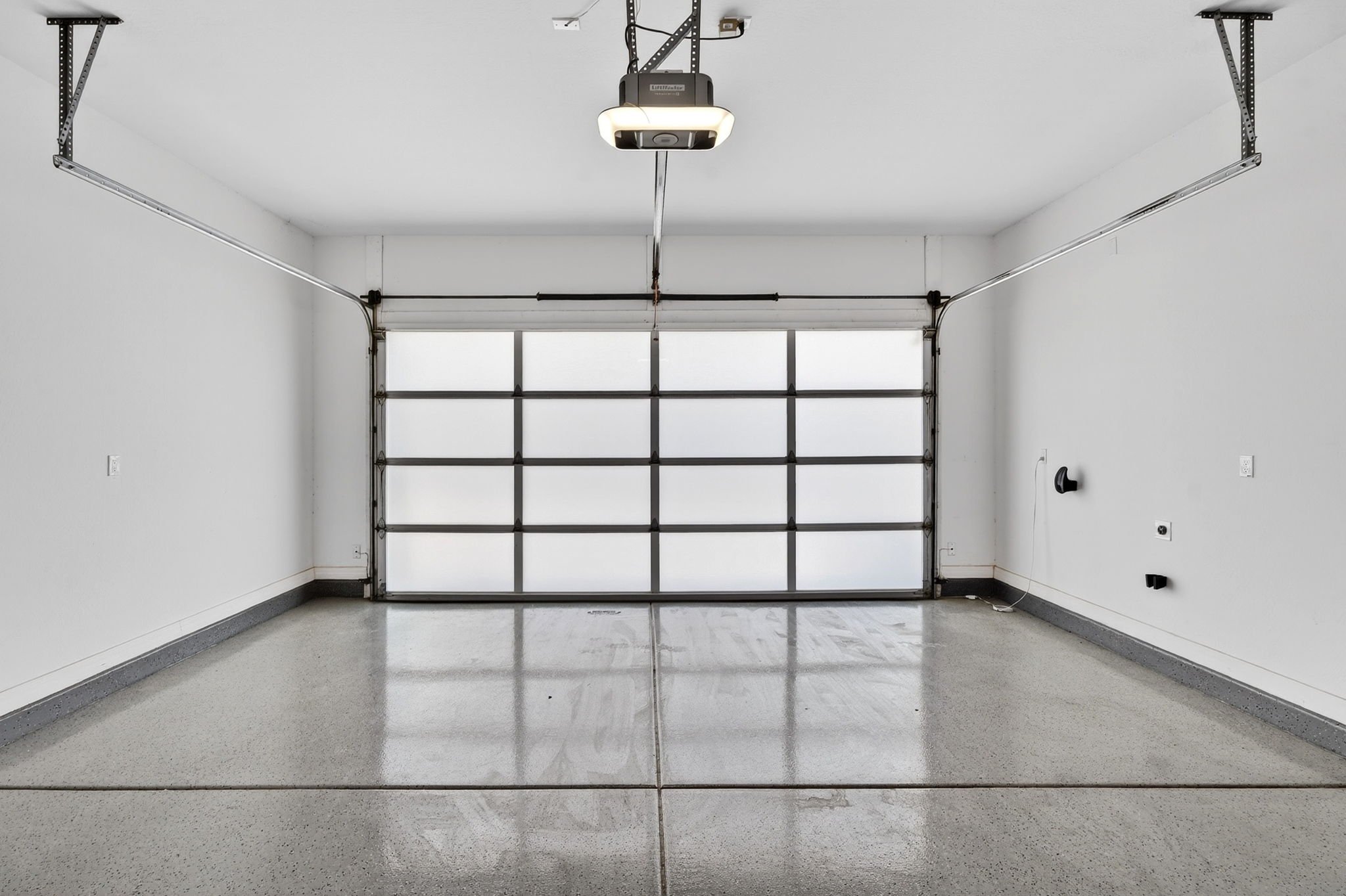 Empty garage with a closed white garage door and a ceiling-mounted garage door opener.