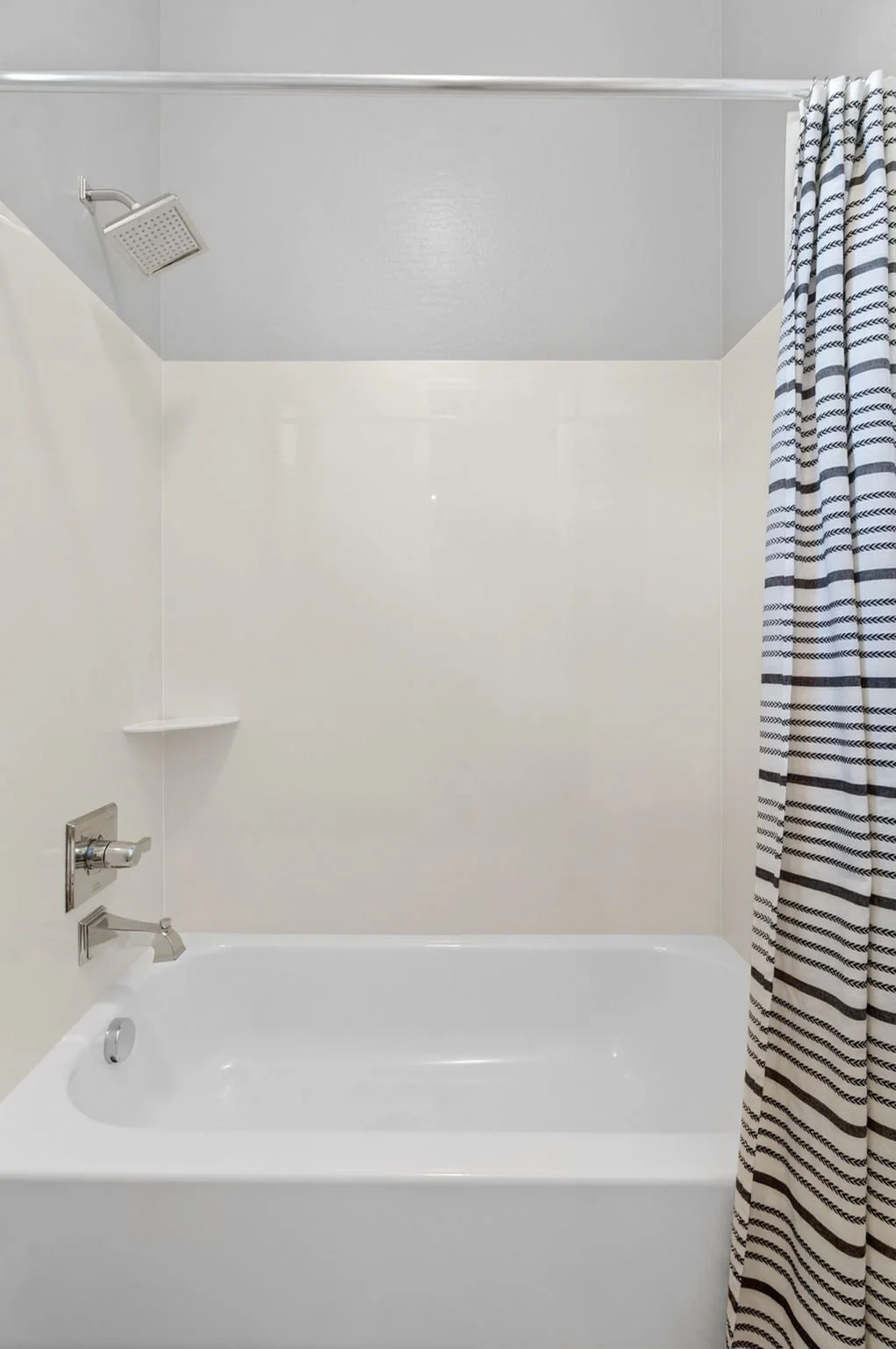 Empty bathroom bathtub with showerhead, faucet, and striped shower curtain.