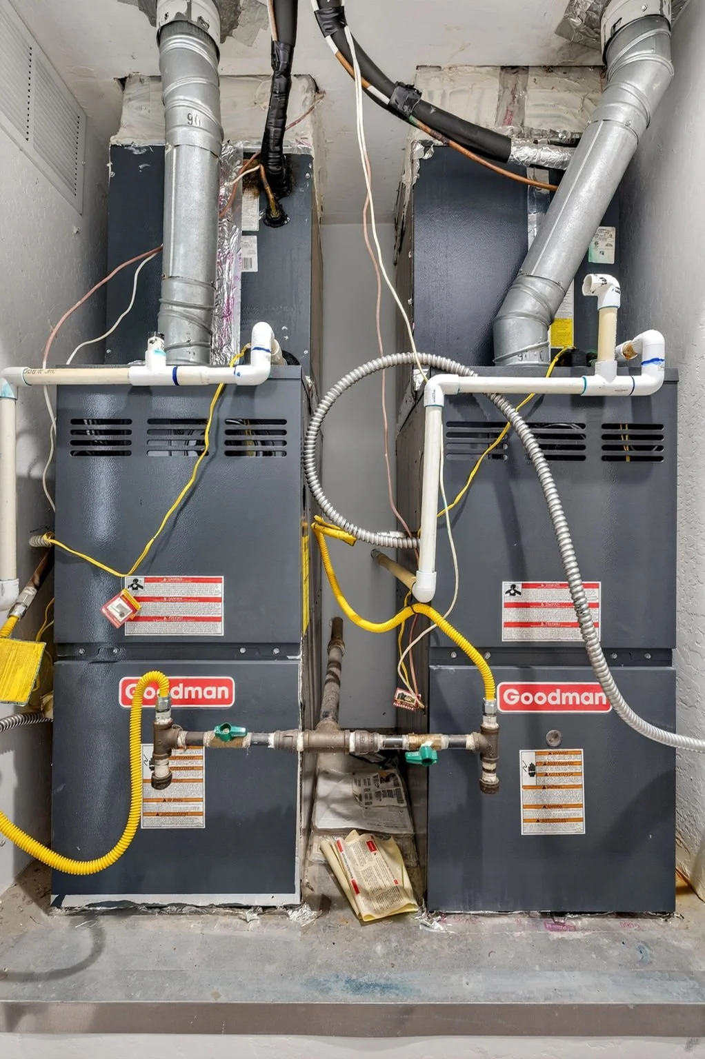 Two Goodman HVAC units with ductwork, pipes, and wiring in a utility area.