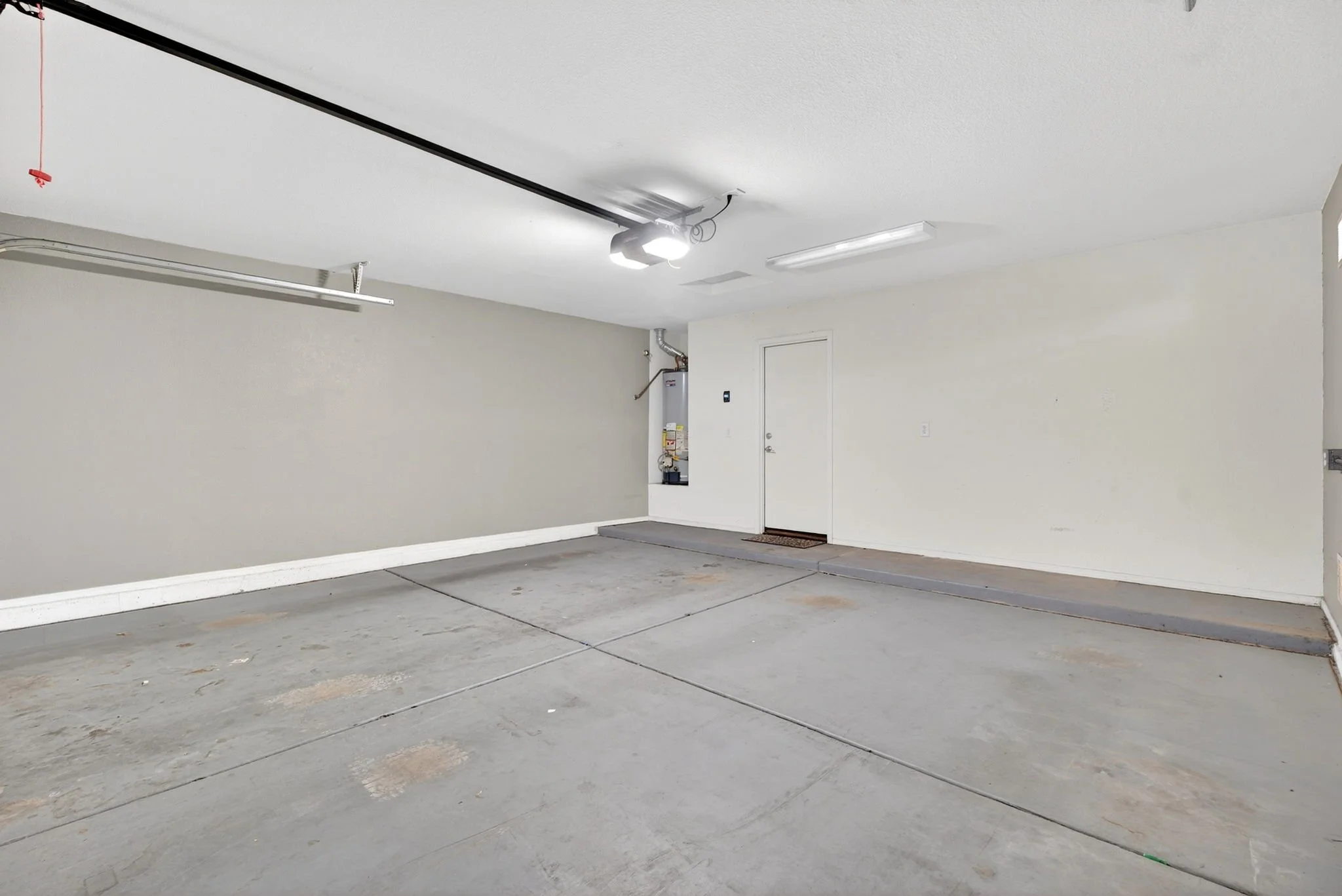 Empty garage with gray concrete floor, white walls, ceiling-mounted lights, and a water heater in the corner.