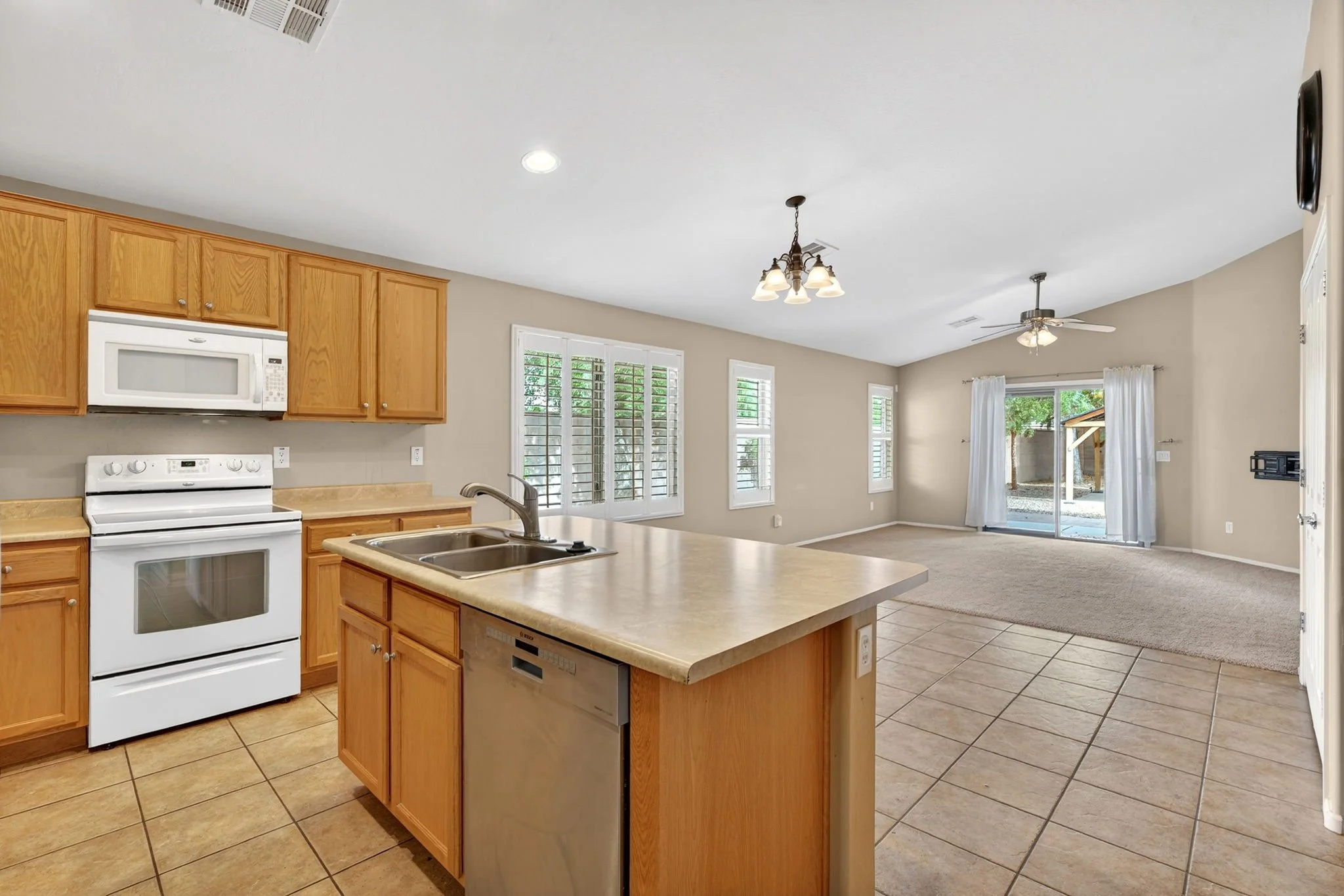 Open-concept kitchen and living area with wooden cabinets, white appliances, tiled floor, multiple windows, and sliding glass door leading outside.
