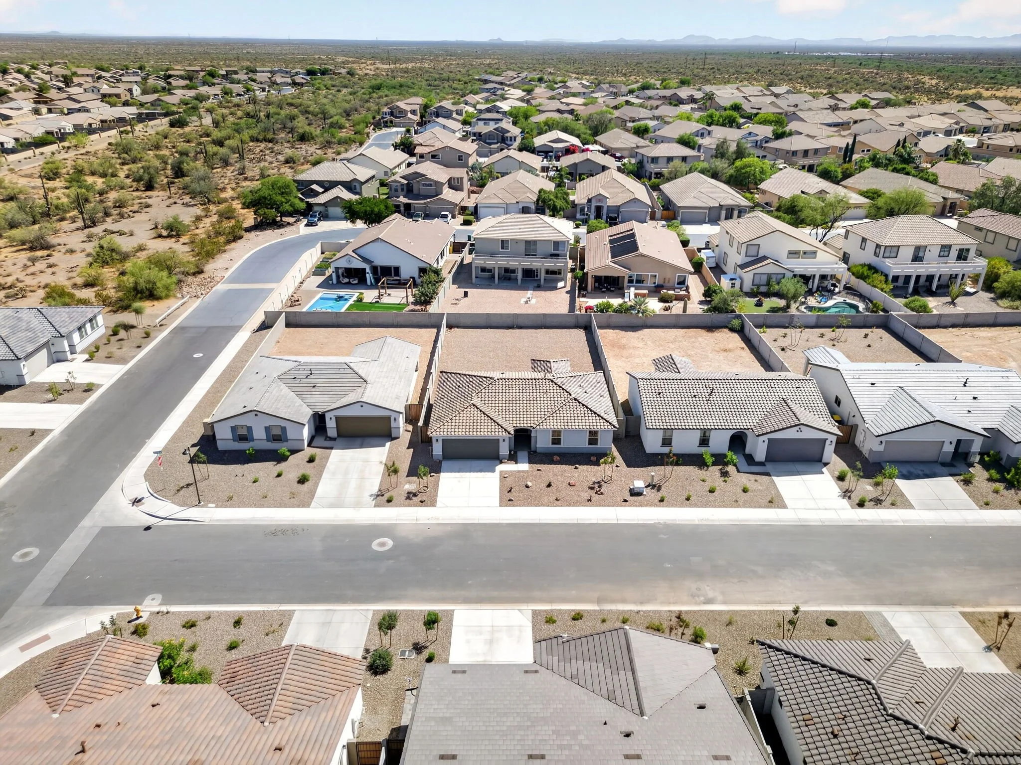 Aerial view of suburban neighborhood with houses, driveways, and backyards, with desert landscape and mountains in the background.