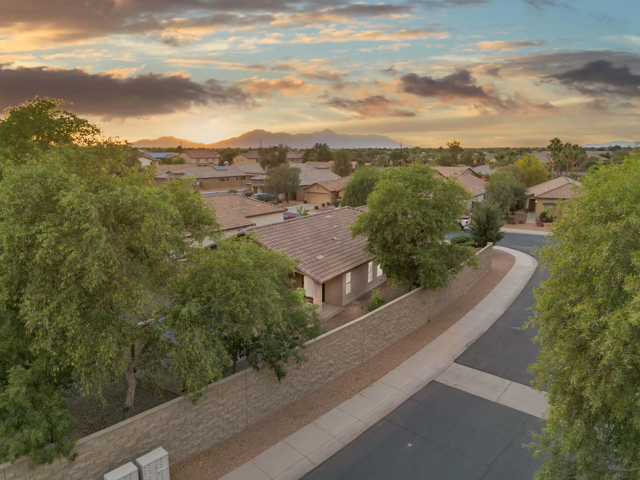 Sunset over a residential neighborhood with houses, trees, and mountain in the background.